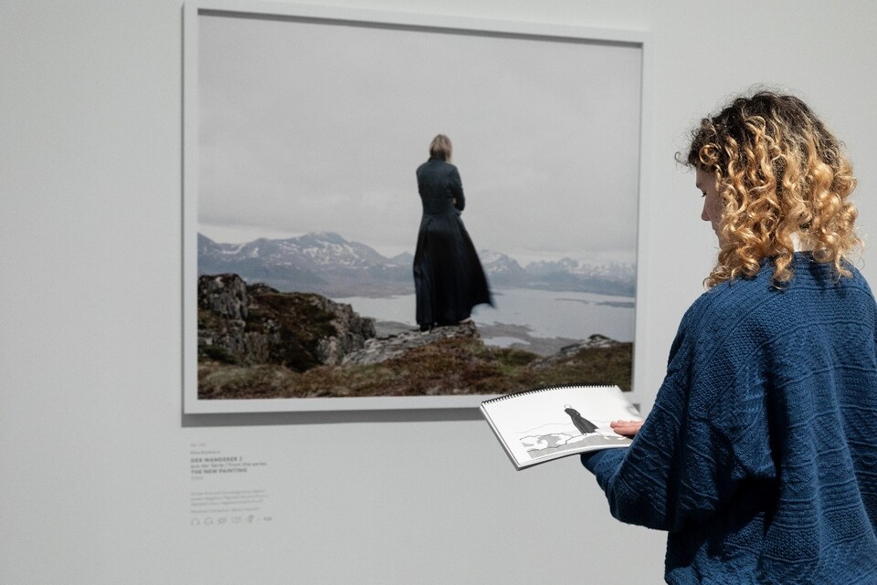 Eine Frau steht vor der Fotografie Der Wanderer II aus der Serie the New Painting, 2004 von Elena Brotherus. In ihren Händen hält sie eine Tastkopie zur Fotografie, die sie mit einer Hand ertastet.Hamburger Kunsthalle, Foto: Fred Dott Eine Frau steht vor der Fotografie Der Wanderer II aus der Serie the New Painting, 2004 von Elena Brotherus. In ihren Händen hält sie eine Tastkopie zur Fotografie, die sie mit einer Hand ertastet. Hamburger Kunsthalle,Foto: Fred Dott