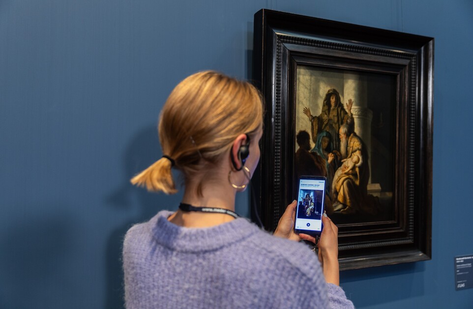 Eine Frau mit Handy und Kopfhörern vor dem Gemälde von Rembrandt Harmensz. van Rijn (1606–1669)