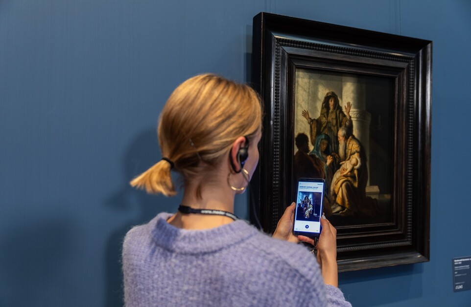 Eine Frau mit Handy und Kopfhörern vor dem Gemälde von Rembrandt Harmensz. van Rijn (1606–1669)