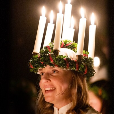 Eine singende Frau in weißem Kleid trägt einen Kranz mit leuchtenden Kerzen, Foto: rechtefrei